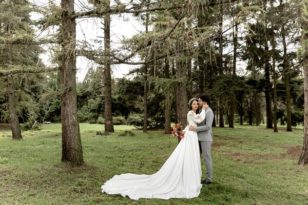 A couple of newlyweds hugging against the backdrop of a green forest. High quality photo