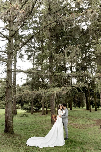 A couple of newlyweds hugging against the backdrop of a green forest — Stockfoto