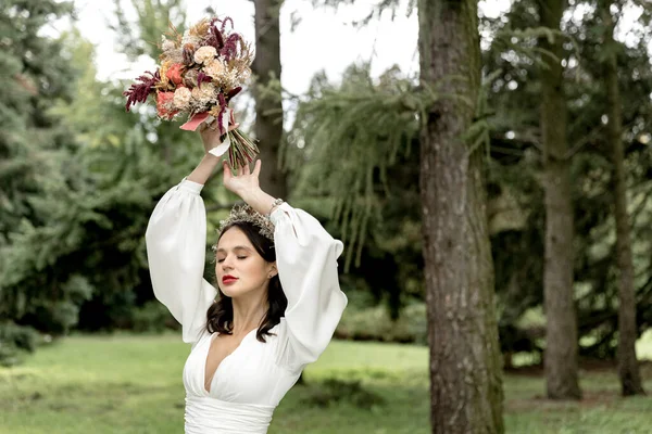 Beautiful bride posing in a wedding white dress holding a bridal bouquet over her head — Stok fotoğraf