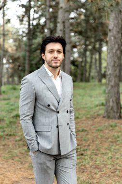 Gri takım elbiseli yakışıklı ve başarılı bir adam ormanın arka planında duruyor. Yüksek kalite fotoğraf