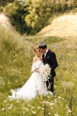 Düğün çifti yeni evliler, tepelerin arkasında şefkatle sarılıp öpüşürler. Yüksek kalite fotoğraf