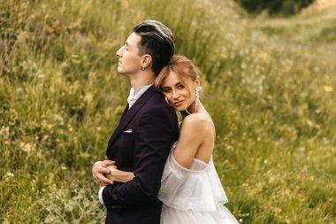 Gelin şık ve yakışıklı damadı kucaklıyor. Doğada güzel bir çift tepenin arkasında. Yüksek kalite fotoğraf