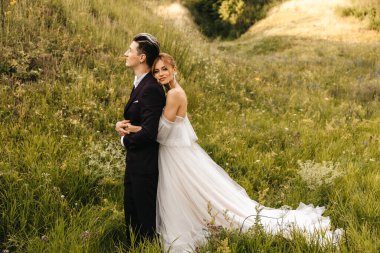 Gelin şık ve yakışıklı damadı kucaklıyor. Doğada güzel bir çift tepenin arkasında. Yüksek kalite fotoğraf