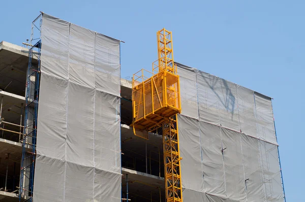 Scaffolding with elevator on facade covered in plastic — Stock Photo, Image