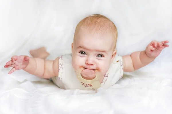 Meisje van de baby op haar buik met handen gespreid en bijtringen in de mond — Stockfoto