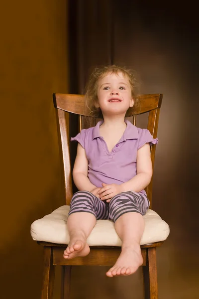 Petite fille souriante assise sur une chaise sur fond intérieur — Photo