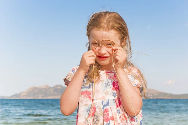 Menina sorridente com óculos imitação de grama seca contra o fundo paisagem mar Imagens Royalty-Free