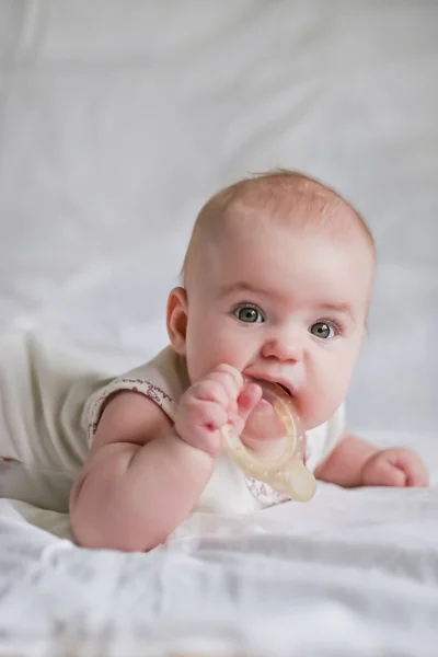 Menina bebê em seu estômago com teether na boca Imagem De Stock