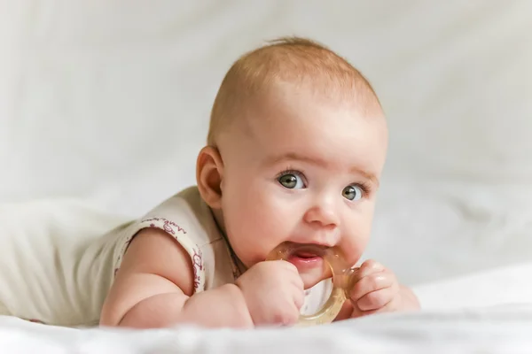 Menina bebê em seu estômago com teether na boca Imagens Royalty-Free