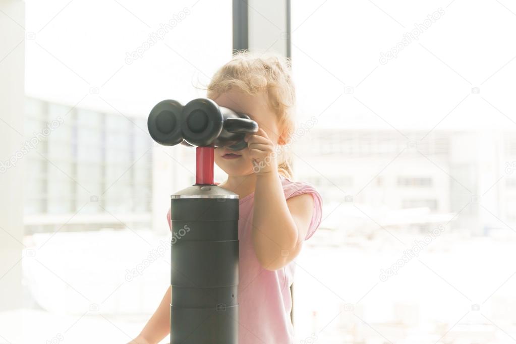 Little girl looking through the binoculars in the window of the airport waiting room