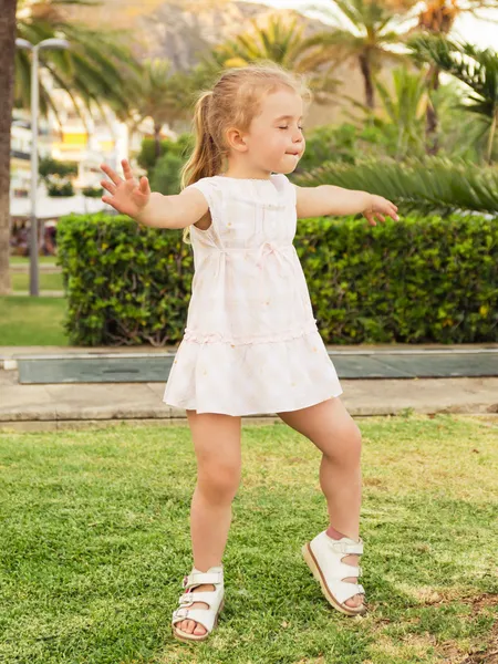 Menina dançando no gramado com os olhos fechados contra o parque ba Fotografias De Stock Royalty-Free