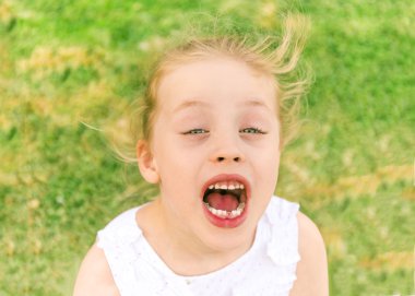 Little girl shouts against green grass background clipart