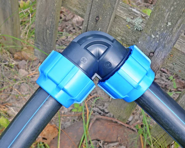 Düşük basınçlı plastik su tedarik sistemi kırsal bölgedeki eski ahşap çitlerin yanında. Açısal plastik uydurma.