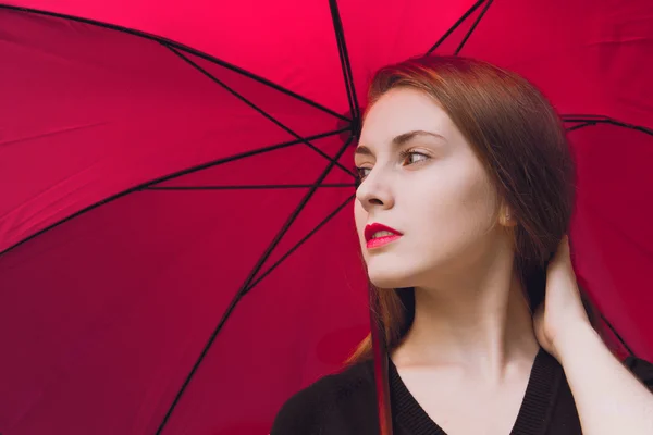 Девушка с красными губами стоит под красным зонтиком — стоковое фото