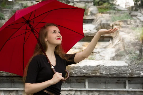 Девушка с красными губами стоит под красным зонтиком — стоковое фото