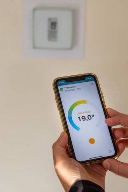 Bir Fransız evindeki termostatı ayarlamak için ellerinde akıllı telefon tutan kişi.
