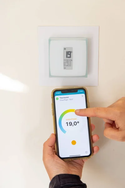 在法国某房子里 手持智能手机调整连接恒温器的人 图库图片