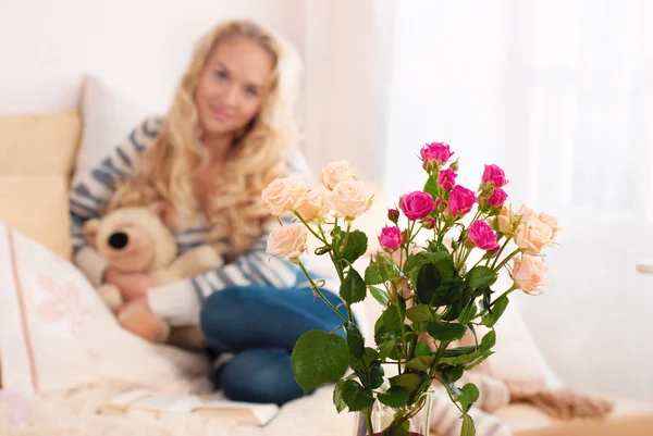 Букет цветов в комнате в интерьере. Счастливая молодая женщина сидит на диване держа кружку дома в гостиной . — стоковое фото