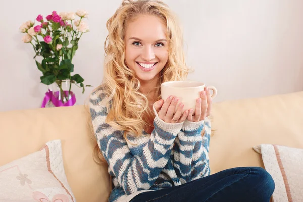 Retrato de uma mulher bonita na sala. Jovem feliz sentada no sofá segurando uma caneca em casa na sala de estar . — Fotografia de Stock
