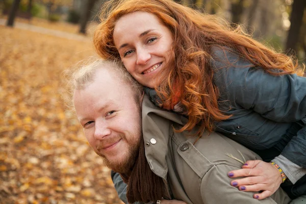 Historia de amor. Autumn Park. Hombre y mujer en un parque de la ciudad cuenta la historia de su amor. Mujer encima de un hombre en su espalda . — Foto de Stock