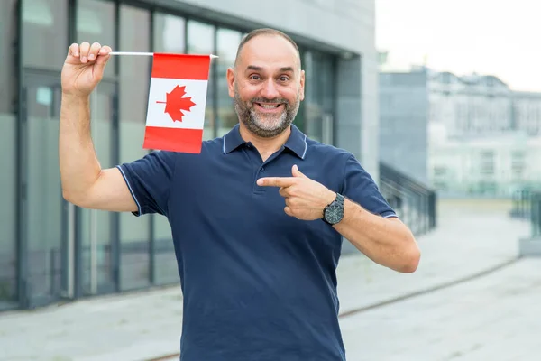 中年男子指着城市背景中的加拿大国旗 加拿大的新生活 — 图库照片