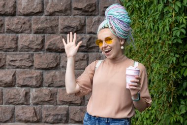 - Merhaba. Rasta saçlı, mutlu genç bir kadın. Elinde yürümek için bir bardak kahve tutuyor..