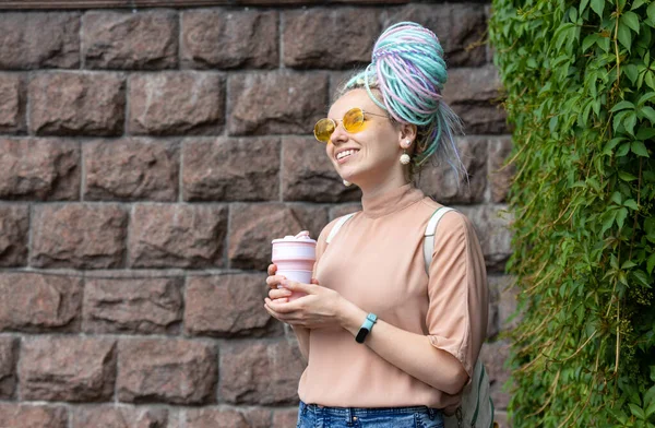 Rasta saçlı mutlu genç kadın yürürken elinde bir bardak kahve tutuyor..