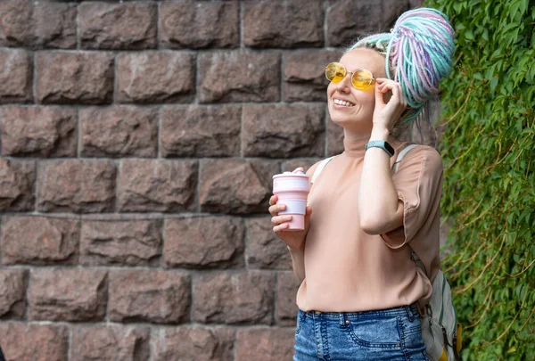 Rasta saçlı mutlu genç kadın yürürken elinde bir bardak kahve tutuyor..