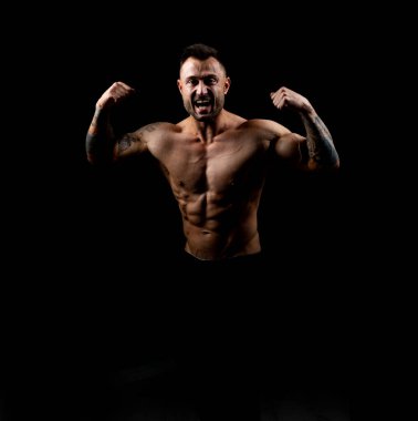 Çıplak gövdeli güçlü bir erkek vücut geliştirici kollarındaki ve vücudundaki siyah arka planda duran kaslarının rahatlığını gösteriyor. Şampiyon.