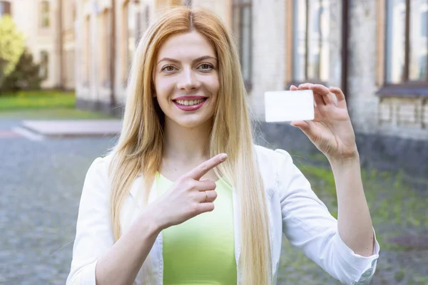 Beautiful business woman points to a white business card in her hand. Mockup for inserting a credit card or student ID.