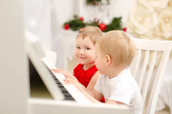 Pojke och flicka som leker på vit piano — Stockfoto