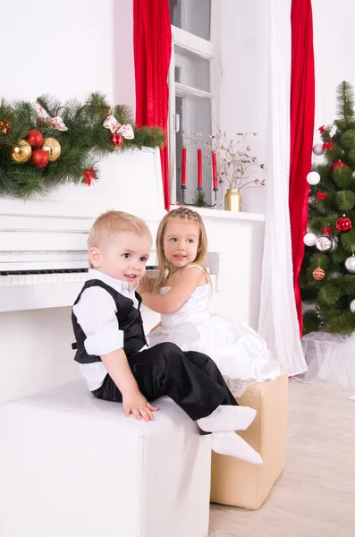 Menino e menina sentados perto de piano branco — Fotografia de Stock