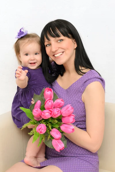 Liten flicka i armarna på sin mor. hålla blommor — Stockfoto