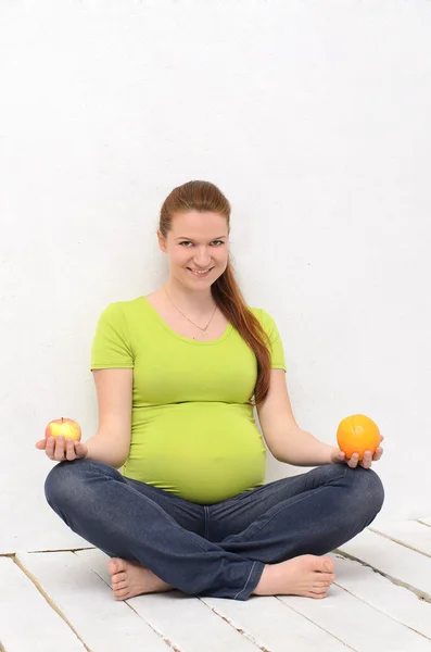 Embarazada sosteniendo una naranja y una manzana — Foto de Stock