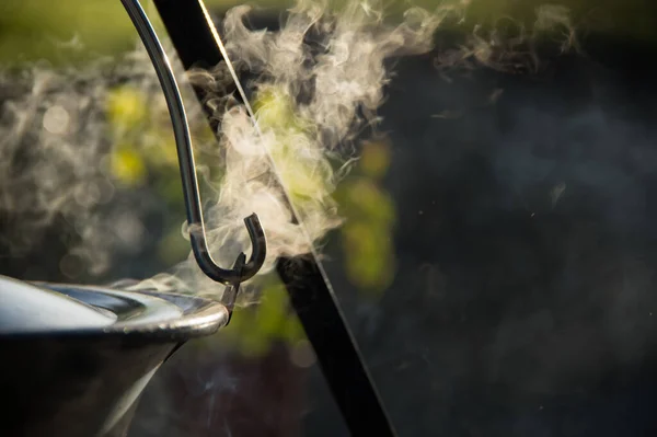 Kamp ateşinin üzerinde buharlı çaydanlık, ateş kasesinin üstünde çaydanlık.