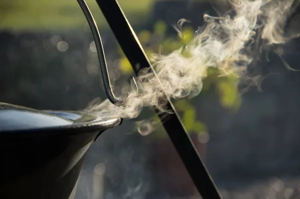 Kamp ateşinin üzerinde buharlı çaydanlık, ateş kasesinin üstünde çaydanlık.