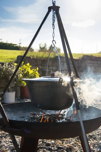 Kamp ateşinin üzerinde buharlı çaydanlık, ateş kasesinin üstünde çaydanlık.