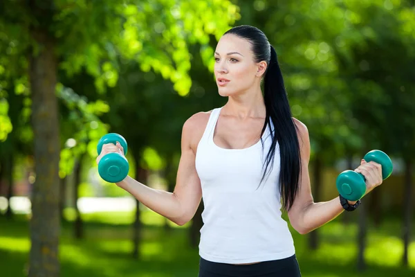 Retrato de mujer alegre en ropa de fitness haciendo ejercicio con mancuerna, al aire libre —  Fotos de Stock