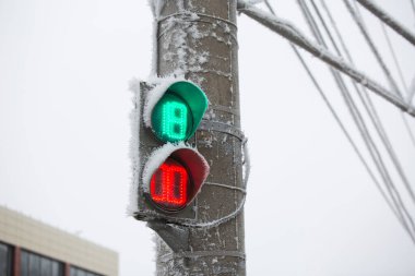 Arka planda elektrik kabloları ve mavi gökyüzü olan donmuş bir trafik ışığının görüntüsü. Kışın buzlu bir yolda meydana gelen kazaların sayısı artar