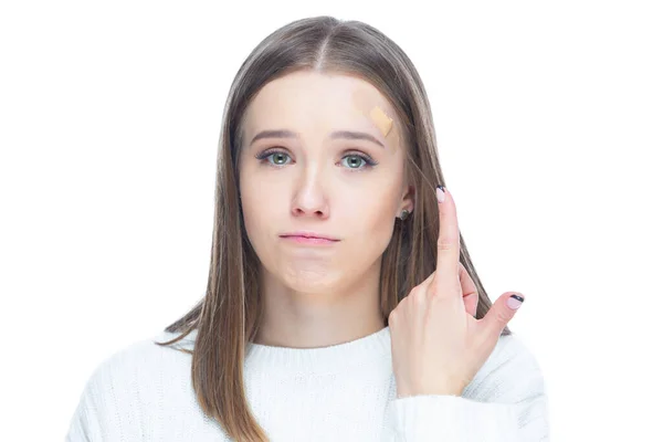 Nahaufnahme einer jungen verängstigten Frau, die nach einer Verletzung auf weißem Hintergrund mit dem Finger auf einen Klebeverband an der Stirn zeigt — Stockfoto