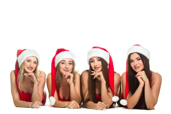 크리스마스. 산타클로스 모자를 쓰고 바닥에 누워 하얀 배경에 고립된 카메라를 보고 있는 네 명의 아름다운 금발 과 갈색 머리 여자 친구의 모습 — 스톡 사진