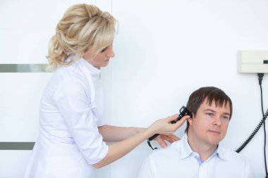 Bir otorhinolaryngolog hastanede otoskoplu bir erkek hastanın dış işitme kanalını inceliyor.