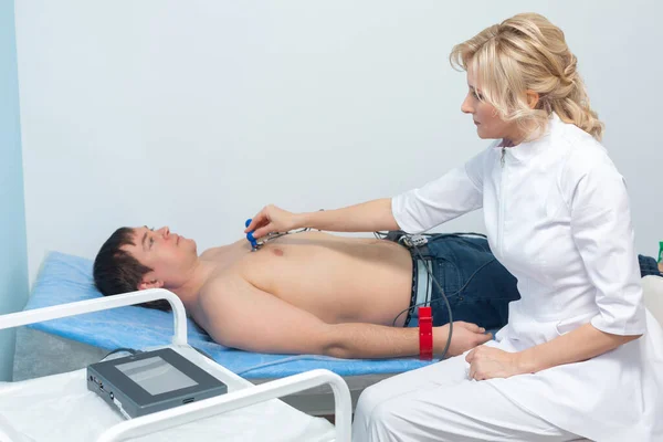 Egy kardiológus orvos érzékelőket alkalmaz egy férfi meztelen testén, aki egy kórházi elektrokardiográfiás eljárás során fekszik a kanapén. — Stock Fotó