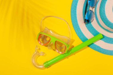 Sarı arka planda plaj aksesuarları, çizgili mavi şapka ve dalış maskesi. Plaj tatili kavramı, deniz turu, sıcak güneşli yaz. Reklam alanı