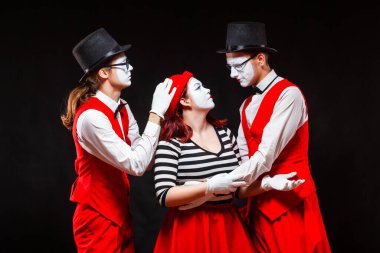 Siyah arka planda izole edilmiş üç pandomim sanatçısının portresi. Bir erkek, bir erkekle bir kadının kafalarını bir öpücükle birleştirir. Tedarik sembolü, Aşk Tanrısı, çöpçatan.