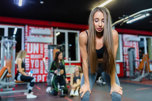 Dziewczyny relaksujące się po treningu i obserwujące jak dziewczyna wykonuje ćwiczenia squat z ostatnią siłą na siłowni — Zdjęcie stockowe