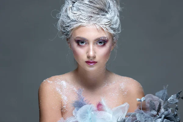 Winter Beauty Femme vêtue de fleurs gelées recouvertes de givre, avec de la neige sur le visage et les épaules. Maquillage fille de Noël. Maquille la Reine des neiges. Isolé sur un fond gris. — Photo