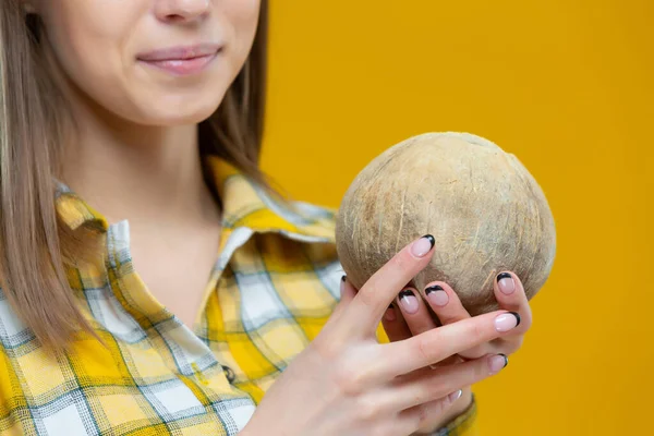 Gros plan d'une noix de coco dans les mains d'une jeune jolie femelle isolée sur fond jaune. Concept de mode de vie sain, bonne nutrition, alimentation, végétalien, végétarien — Photo