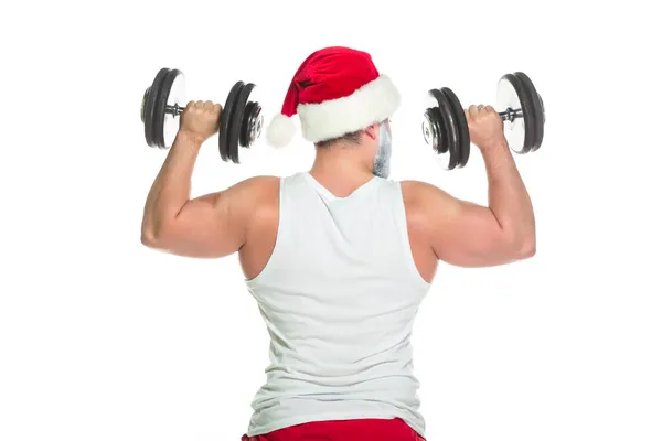 Navidad. Vista posterior de atleta musculoso fuerte en un disfraz de Papá Noel levantando pesadas mancuernas mostrando sus bíceps aislados sobre fondo blanco — Foto de Stock