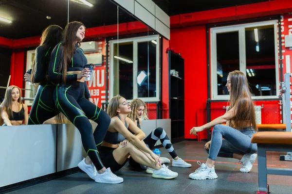 Vier müde, fröhliche athletische Mädchen plaudern und entspannen sich nach einem harten Training im Fitnessstudio — Stockfoto